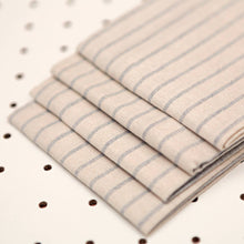 Load image into Gallery viewer, Stack of beige fabric with blue stripes on a white pegboard background