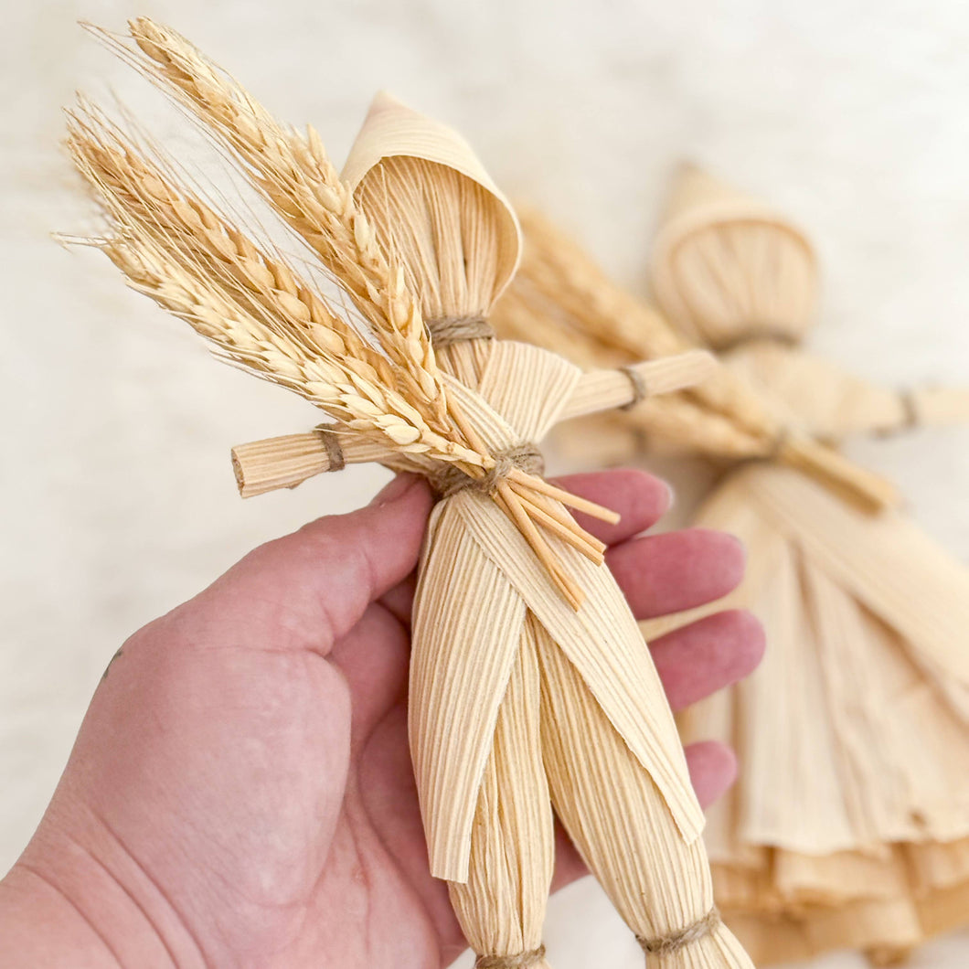Hand holding a bundle of dried corn husks with more husks in the background on a light surface.