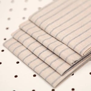 Stack of beige fabric with blue stripes on a white pegboard background