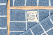 Load image into Gallery viewer, Blue and white checkered towel with a wooden border and meema label.
